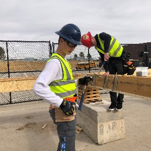 Two students work on constructing the floor of a new house.